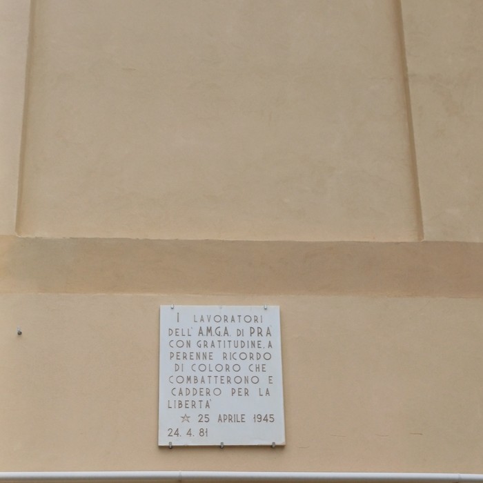 Lapide in marmo con iscrizione, affissa su una parete esterna intonacata.