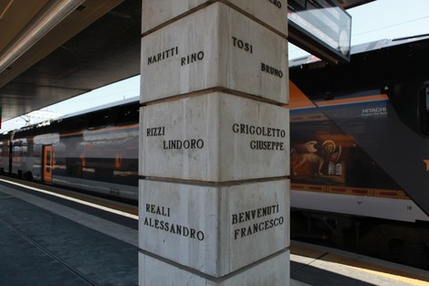 Monumento ai ferrovieri caduti per la libertà, con nomi incisi su colonna in pietra, sullo sfondo un treno.