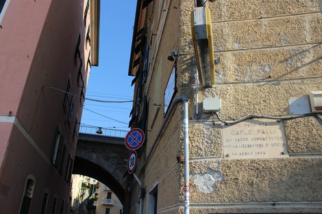 Lapide commemorativa in un vicolo, con dettagli architettonici e un ponte sullo sfondo.
