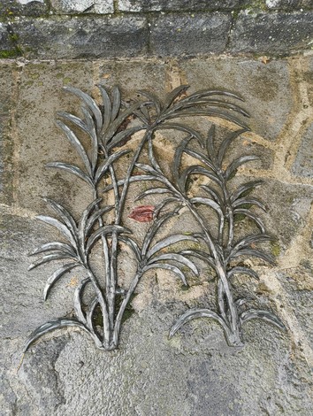 Dettaglio del "Monumento a Comini", caratterizzato da elementi floreali in metallo su una base di pietra.