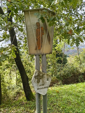 Pannello della Via Crucis di Casaglia, immerso nel verde, con un'immagine di Gesù spogliato.