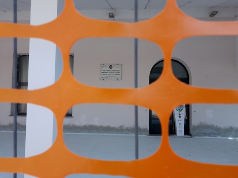 Lapide commemorativa visibile attraverso una recinzione arancione in un edificio.