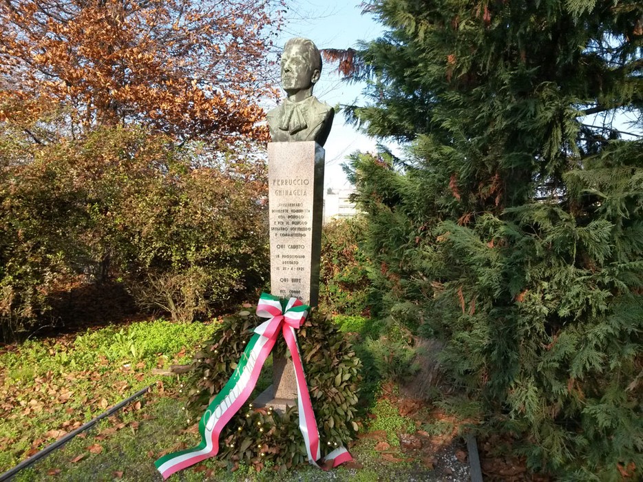 Monumento a Ghinaglia con busto e decorazioni, immerso nel verde, in memoria di un'importante figura storica.