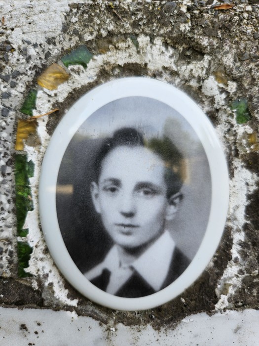 Ritratto in bianco e nero di un giovane, incastonato in una cornice ovalizzata, su un cippo di Gualdi.