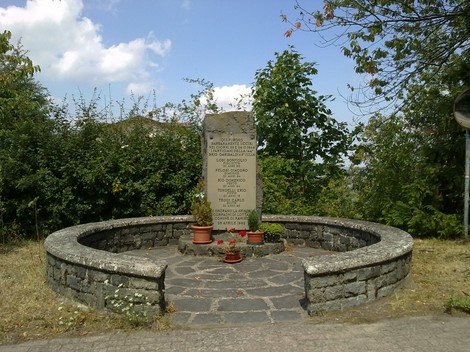 Monumento commemorativo immerso nel verde, dedicato ai caduti di Bora, con dedica incisa su una stele.