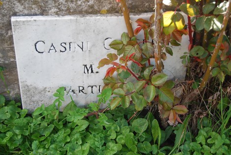 Targa commemorativa nel Parco della Resistenza di Caniparola, circondata da piante e vegetazione.