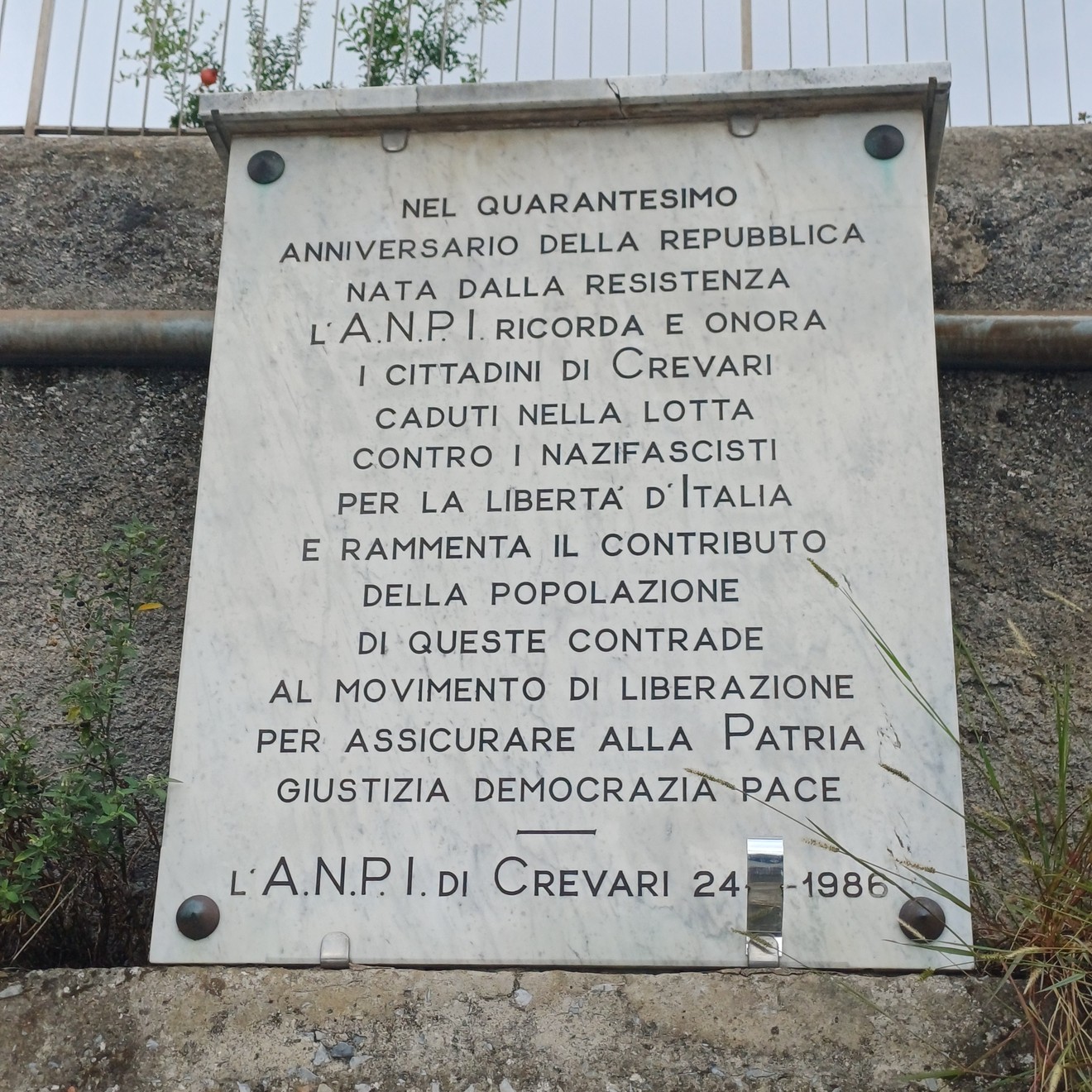 Lapide in marmo con iscrizione, fissata a una parete esterna in pietra.