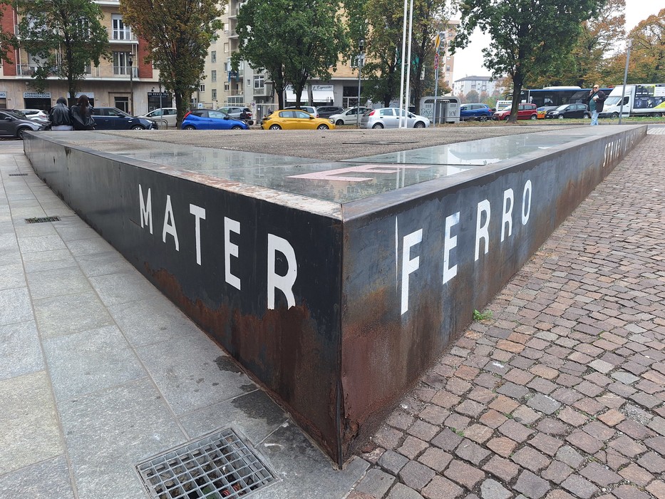 Monumento in acciaio corten a forma di basamento angolare, con iscrizioni incise, in una piazza lastricata.