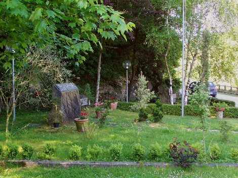 Area monumentale dedicata ai Caduti di Partina, immersa nel verde, con piante e fiori commemorativi.