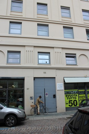 Lapide commemorativa sulla facciata di un edificio, con una persona in bicicletta che si ferma.