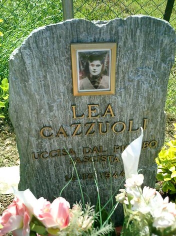Cippo commemorativo di Lea Cazzuoli con fotografia e fiori, situato in un'area verde.