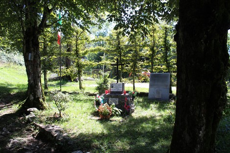 Monumento a Gotti circondato da alberi, fiori e bandiera italiana in un ambiente verde e tranquillo.