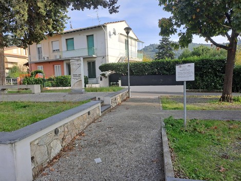 Monumento a Cosci, situato in un giardino pubblico circondato da edifici e alberi, simbolo di memoria e cultura locale.