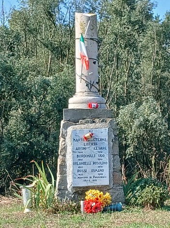 Cippo commemorativo dedicato a Arfini, Bordonali, Orlandelli e Rossi, circondato da natura e fiori.
