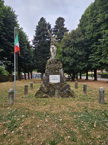 Monumento ai Caduti di Stagno Lombardo, circondato da alberi e cimeli, con una statua che commemora i caduti.
