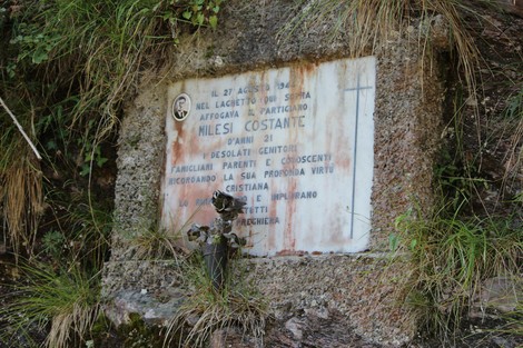 Lapide commemorativa dedicata a Milesi Costante, situata in un ambiente naturale.