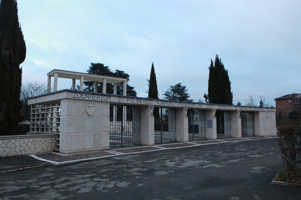 Ingresso del Cimitero di guerra polacco, caratterizzato da architettura sobria e alberi. Atmosfera di rispetto e memoria.
