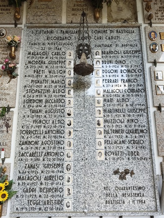 Lapide commemorativa con nomi di caduti per la Libertà, adornata da fiori e photo di persone onorate.