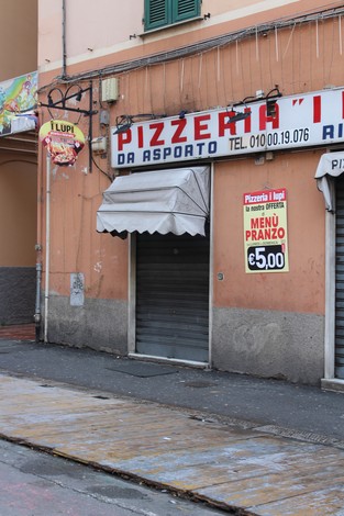 Pizzeria con insegna alta e chiusura avvolgibile, situata lungo una strada con pavimentazione in legno.