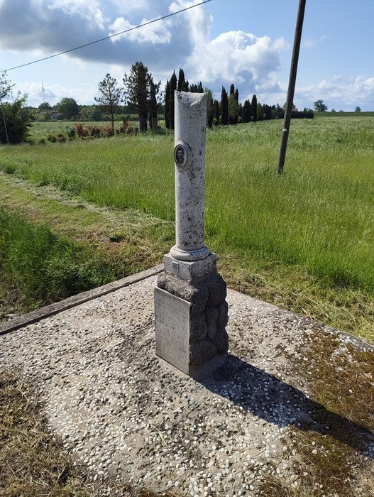 Cippo a Brandoli in un paesaggio verde, con alberi sullo sfondo e cielo sereno. Dettagli di pietra e storia.