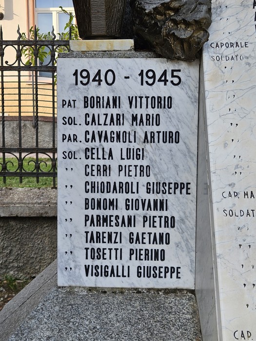 Lapide in marmo bianco con lungo elenco di nomi, inserita in un monumento all'aperto vicino a una cancellata.