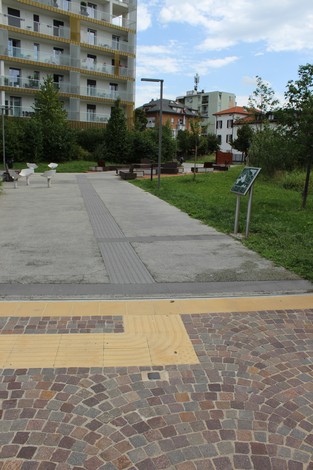 Pietra d'inciampo dedicata a Barnaba di Buja in un contesto urbano con panchine e verde.