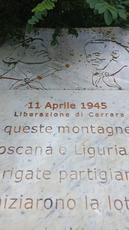 Stele commemorativa dedicata alle Brigate Partigiane, con rilievi e iscrizioni storiche, situata in un contesto naturale.