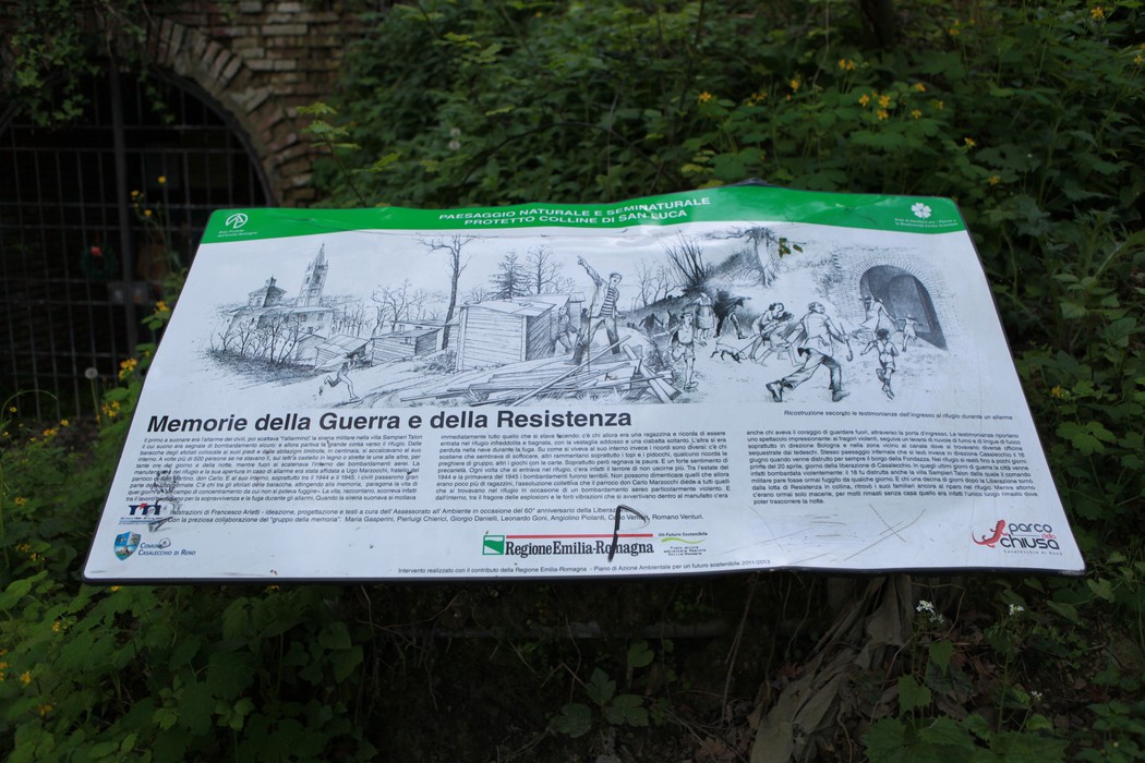 Scorcio del "Sentiero dei Bregoli" con pannello informativo su memorie di guerra e resistenza, immerso nella vegetazione.