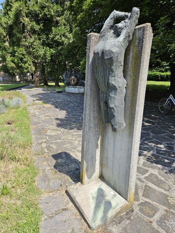 Monumento alla Resistenza, scultura in cemento e bronzo tra vegetazione e pavimentazione di pietra.