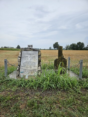 Cippo commemorativo a Favagrossa, circondato da un campo con sparse vegetazione e un cielo nuvoloso.