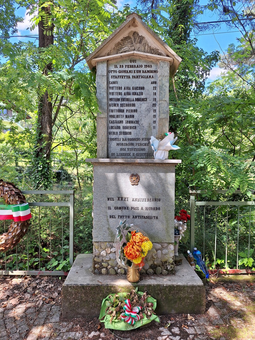 Monumento dedicato ai giovani partigiani, con iscrizioni commemorative e adornato da fiori e simboli tricolore.