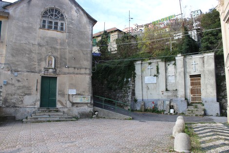 Vista della lapide ai caduti di Aggio, in un contesto di edifici e vegetazione circostante.