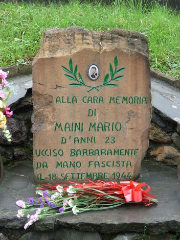 Cippo commemorativo con dedica a Mario Maini, ucciso il 18 settembre 1944, adornato con fiori.