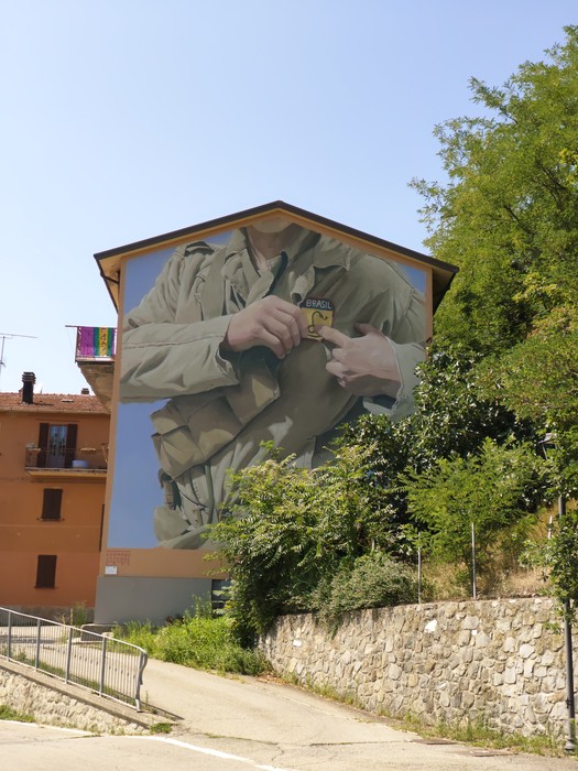 Murale su parete di un edificio, raffigura un soldato in uniforme che appunta una spilla sul petto.