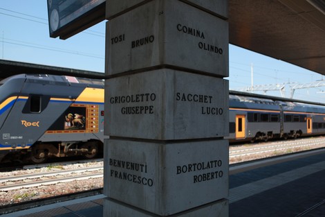 Monumento ai ferrovieri caduti per la libertà, con inscrizioni commemorative e treni in transito.