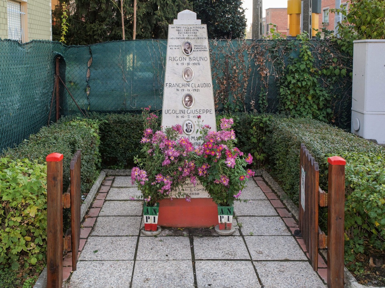 Monumento commemorativo a Rigon, Franchini, Ugolini e Bassoli, circondato da fiori e vegetazione.