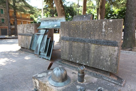Monumento alla Resistenza antifascista, composto da lastre di pietra e elementi in bronzo, immerso nel verde.