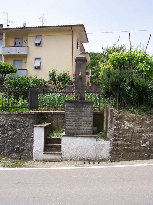 Monumento commemorativo dedicato a Ceccaroni e altri, situato in un contesto urbano e naturale.