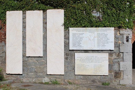 Lapide commemorativa con iscrizioni su marmo e pietra, situata in un contesto storico e artistico.