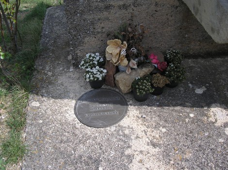 Monumento di Collo Sodo con fiori e lapide commemorativa su una base di pietra.