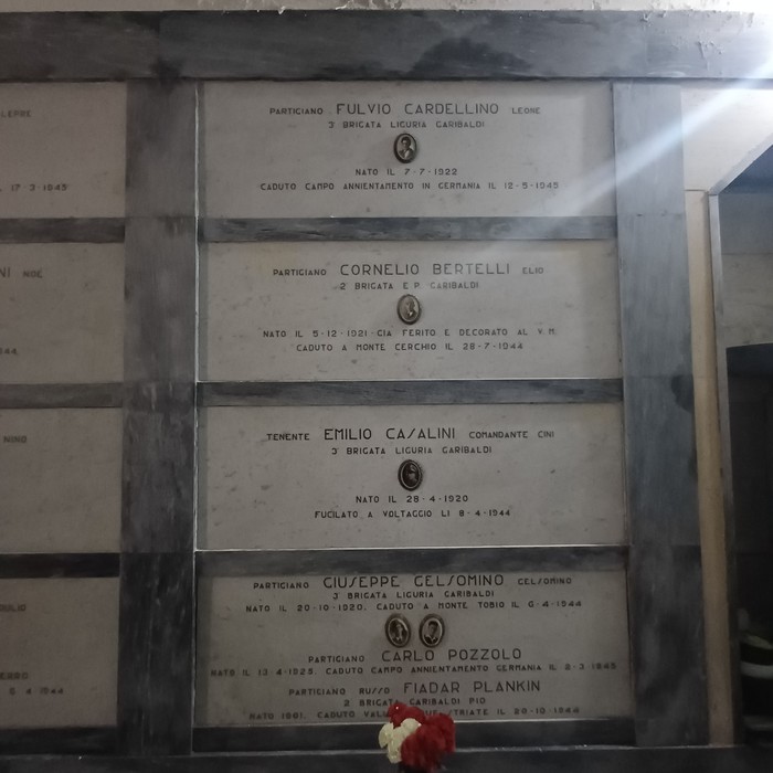 Lapidi marmoree allineate su una parete, ciascuna con iscrizione e piccolo ritratto ovale dei partigiani.