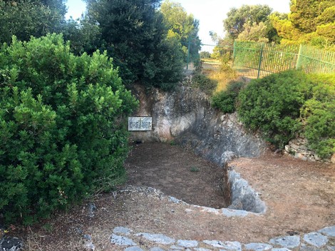 Lapide commemorativa in un'area verde, dedicata alla fossa degli ufficiali, circondata da vegetazione.