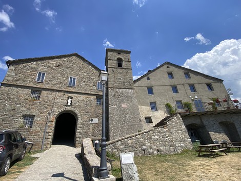 Targa ai Rossi, vista di edifici in pietra con campanile, immersi nel verde sotto un cielo azzurro.