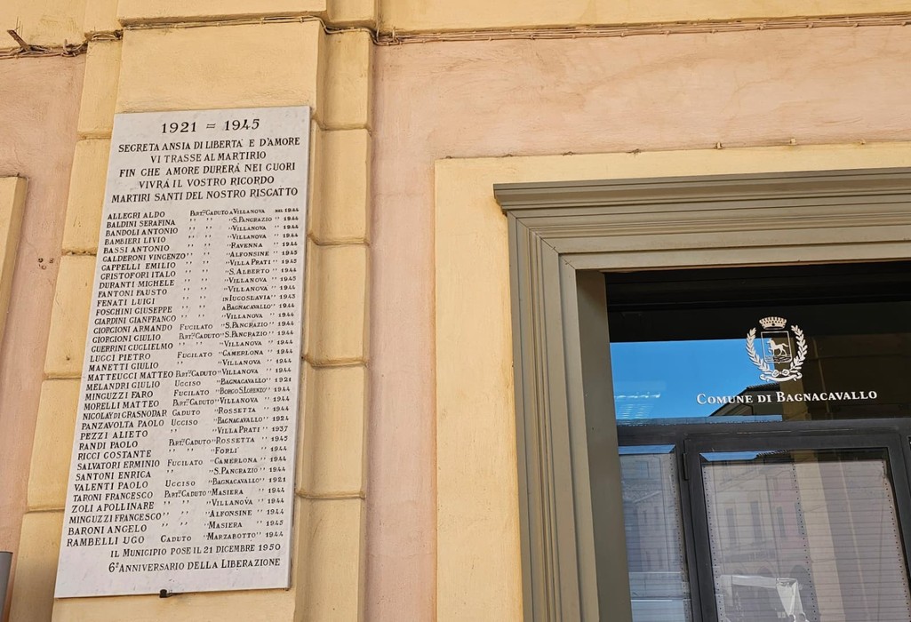 Lapide commemorativa con nomi dei caduti, situata su una parete esterna, in memoria di un conflitto.