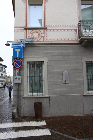 L'angolo di una strada con il cartello dedicato a M. O. Gasparini e dettagli architettonici di un edificio.