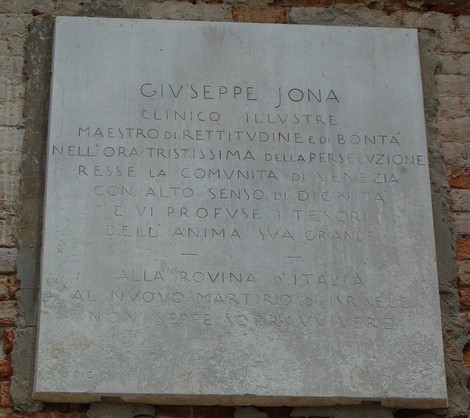 Lapide commemorativa dedicata a Giuseppe Jona, clinico illustre e benefattore, collocata su un muro di pietra.