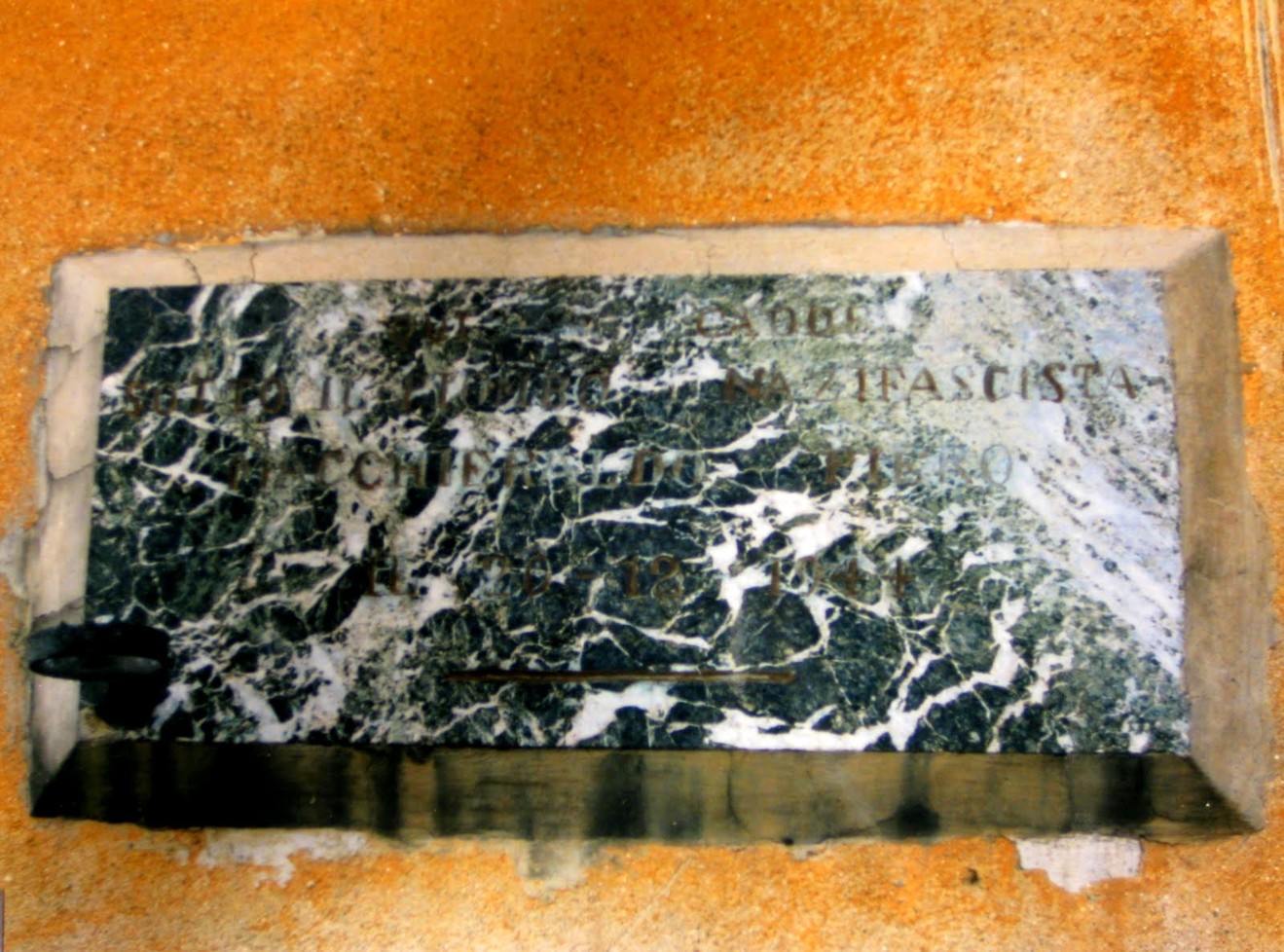 Lapide commemorativa di Macchieraldo, in marmo con decorazioni, situata in un contesto storico significativo.