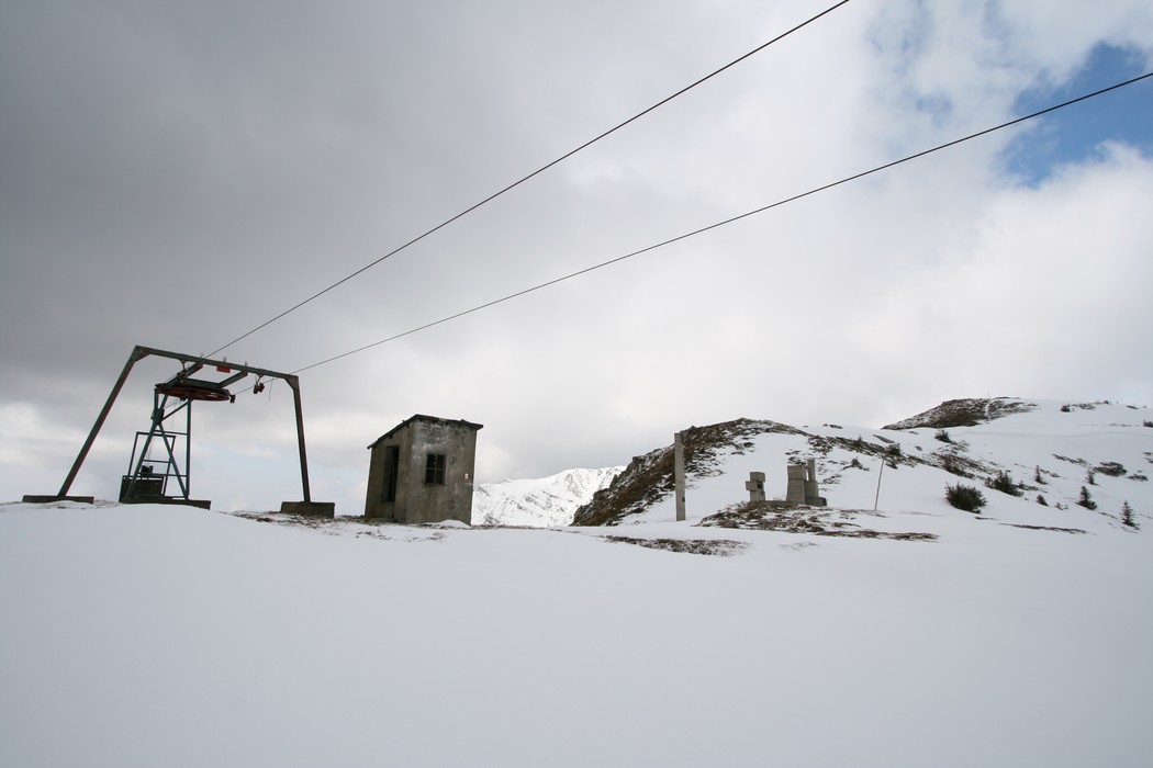 Monumento alla XI Zona "Pippo" in un paesaggio innevato con strutture in rovina e cavi di una seggiovia.