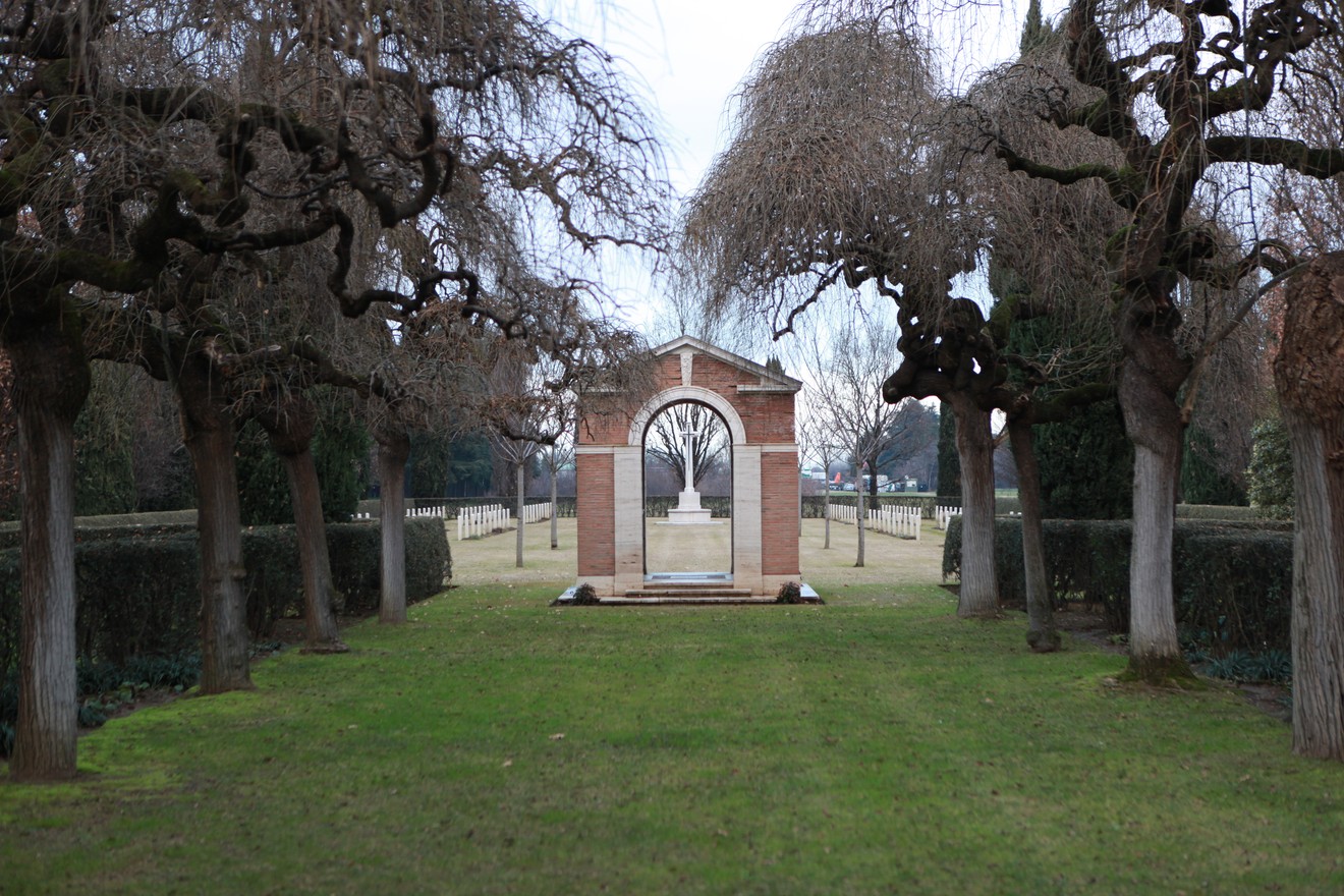 Cimitero di guerra del Commonwealth con alberi e struttura commemorativa in uno spazio verde tranquillo.