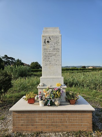 Monumento ai Martiri di Ponte Ruffio con fiori e un paesaggio verde sullo sfondo.